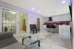 Una sala moderna con una mesa de centro de vidrio, un sofá y una cocina con barra y asientos.