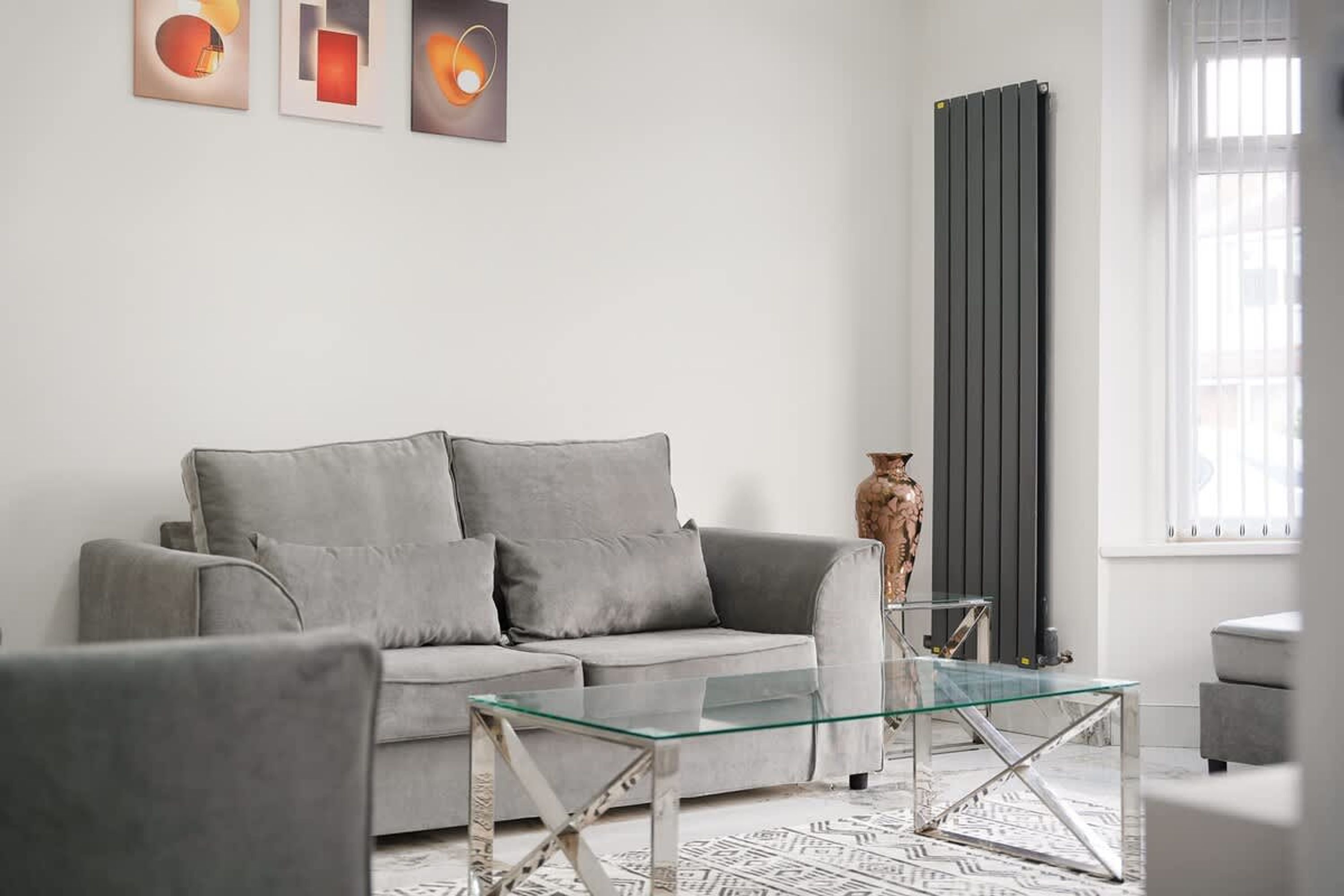 A modern living room with a grey sofa, a glass coffee table, and a radiator.