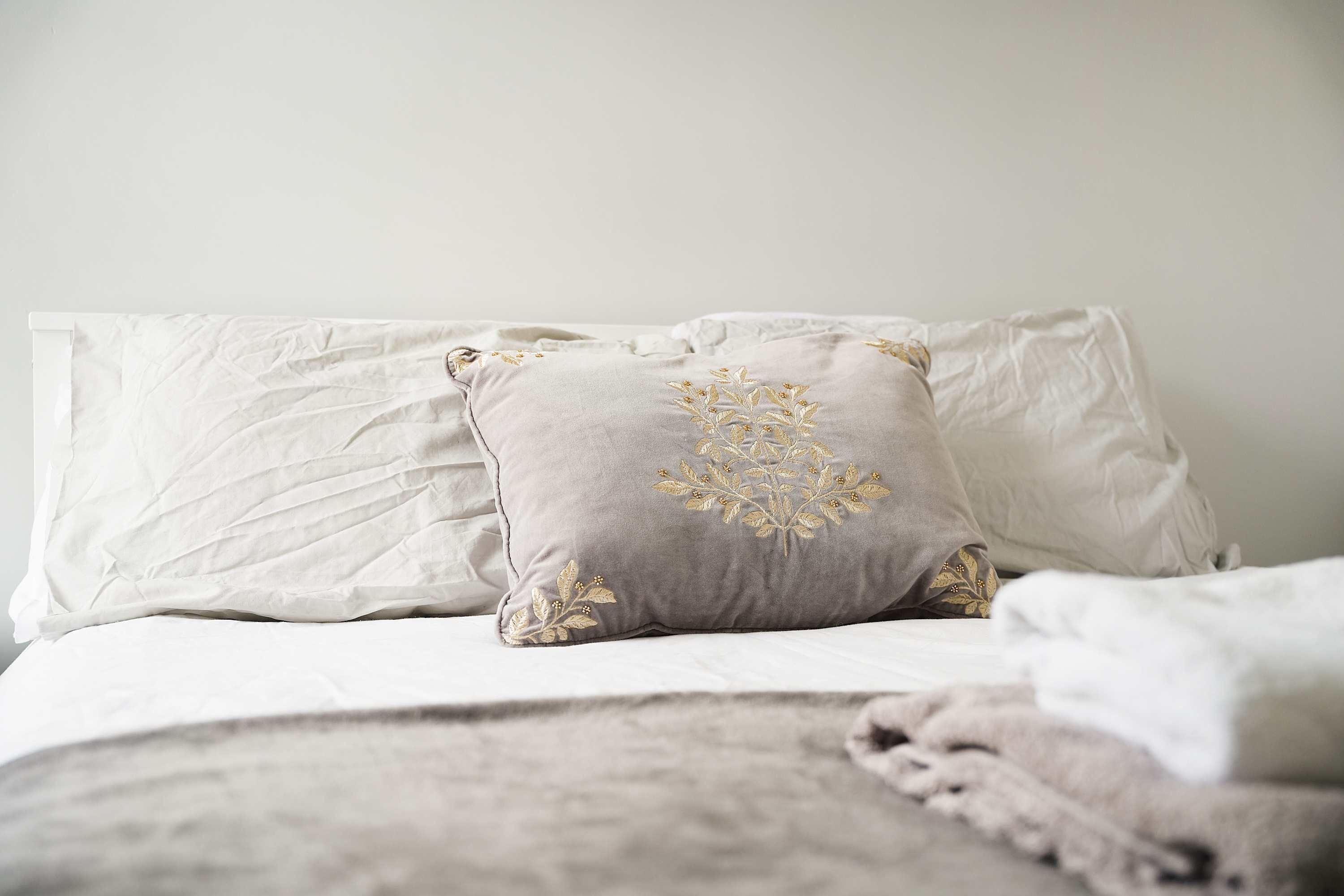 A bed with white and grey pillows, one with a floral embroidered design.