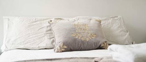 A bed with white and grey pillows, one with a floral embroidered design.