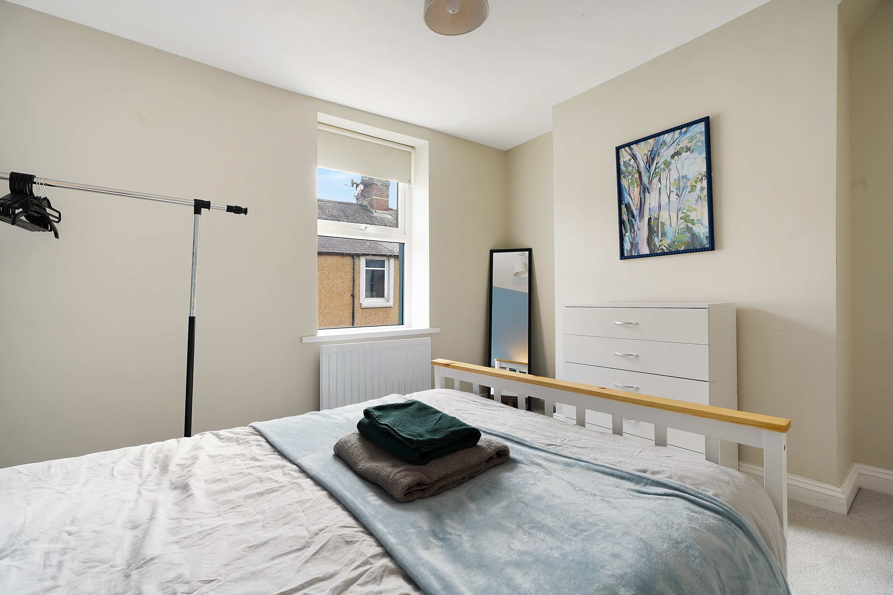 A bedroom with a bed, a radiator, a window, a dresser, and a painting on the wall.