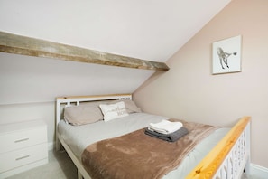 A bedroom with a sloped ceiling, a bed with a wooden headboard, a small bedside table, a drawer unit, and a framed picture on the wall.