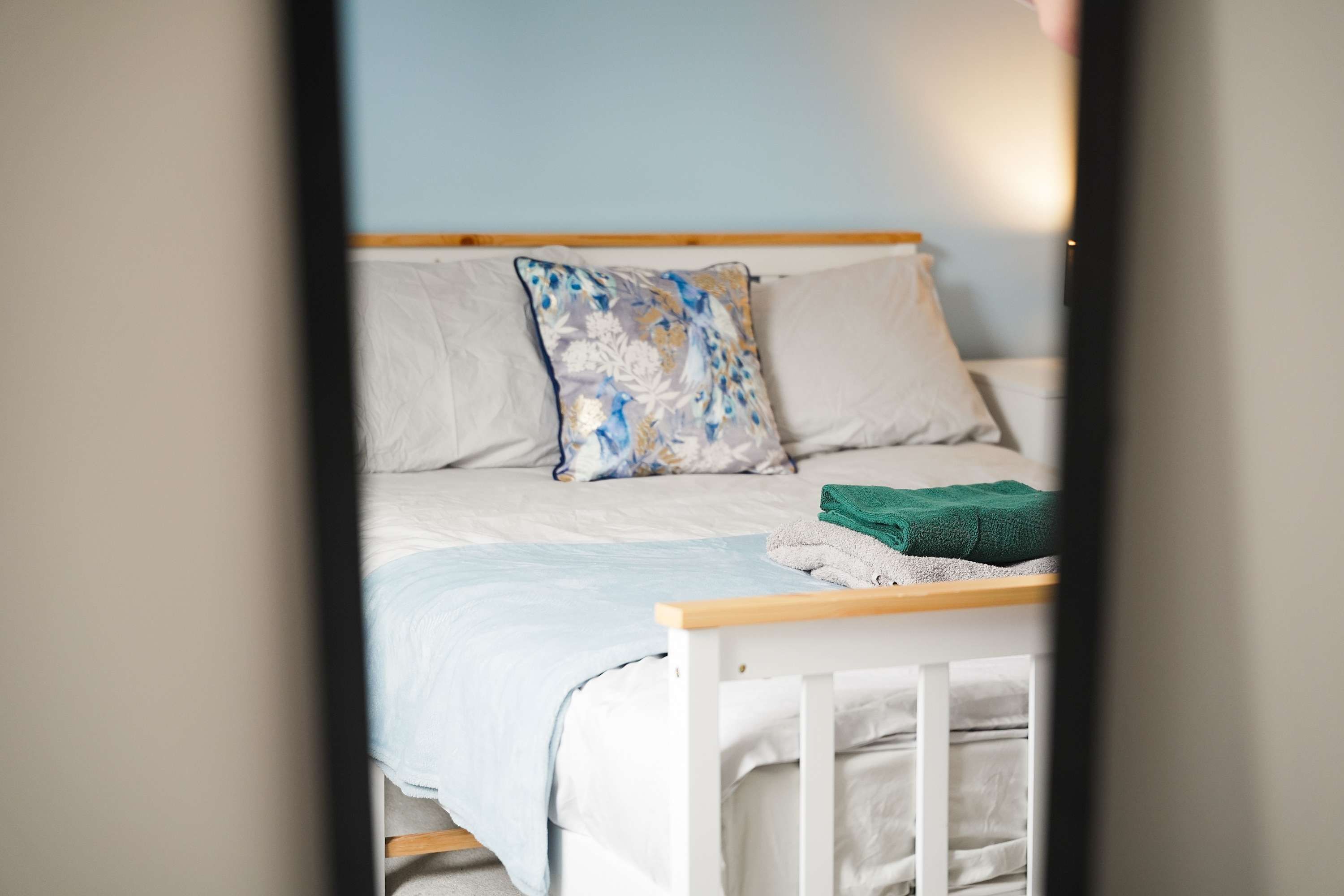 A bed with a wooden headboard, white bedding, and a floral pillow.