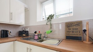Une cuisine équipée d’un évier, d’une bouilloire, d’un grille-pain et d’une pancarte indiquant : « Vous êtes les bienvenus pour utiliser notre réseau Wi-Fi. Voici le mot de passe : ».