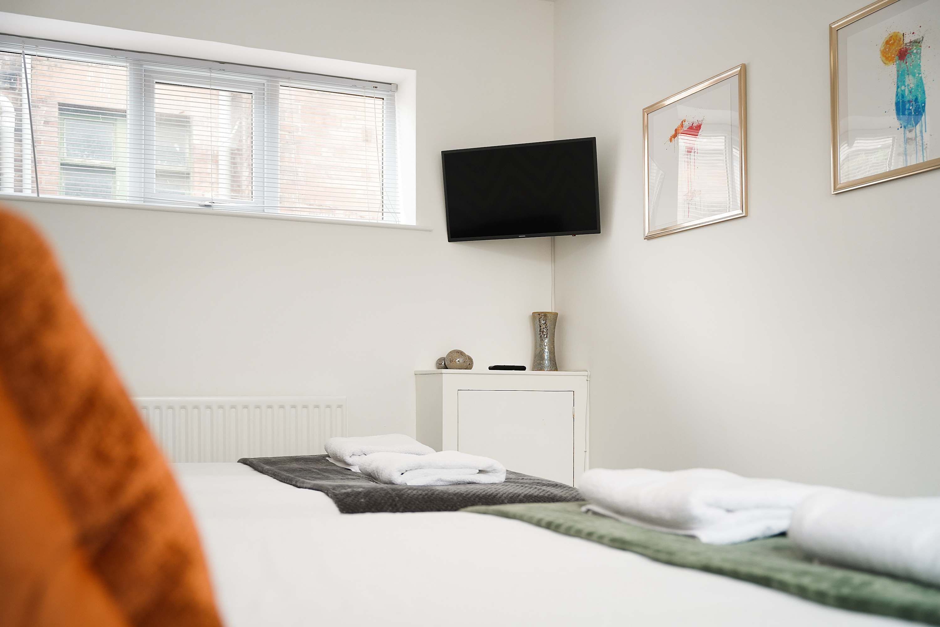 Une chambre d’hôtel avec un lit, un téléviseur fixé au mur et une fenêtre avec des stores.
