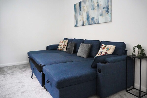 A blue sofa with multiple cushions, a small side table with a plant, and a painting on the wall.