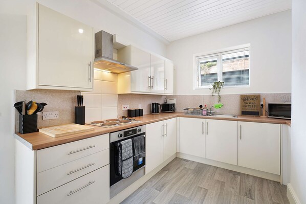 A modern kitchen with white cabinetry, a built-in oven, and a window with blinds.