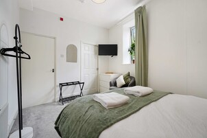 A hotel room with a bed, a TV mounted on the wall, a coat rack, and a window with curtains.