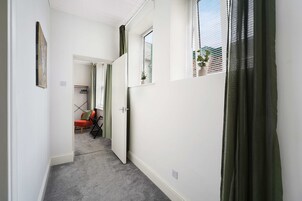 A narrow hallway with a carpeted floor, a door leading to a room, and a window with a plant on the sill.