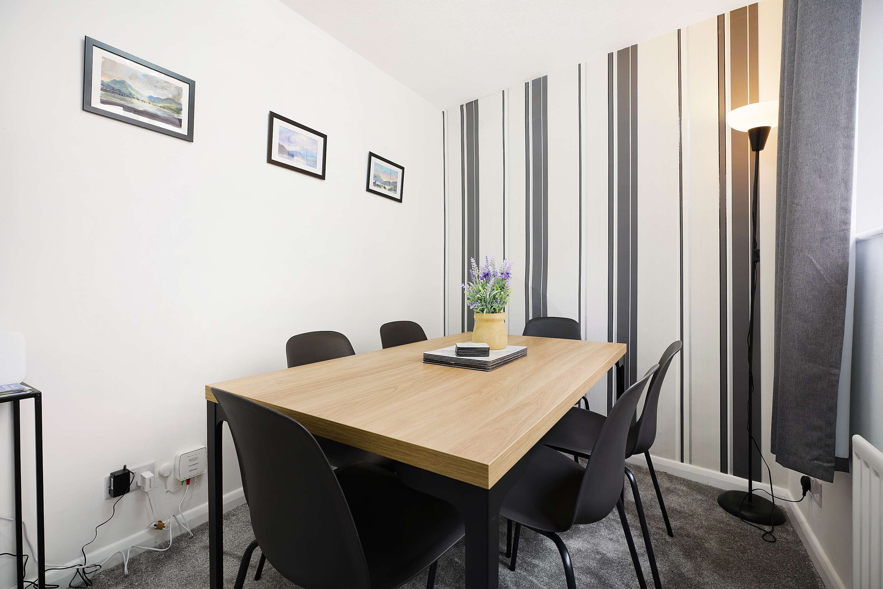 A conference room with a wooden table, black chairs, a vase with flowers, and framed pictures on the wall.