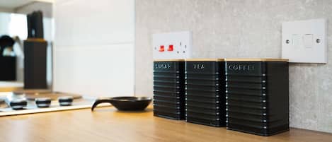 En køkkenbordplade med tre sorte beholdere mærket 'SUGAR', 'TEA' og 'COFFEE'.