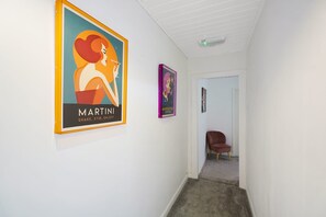 A hallway with two framed posters on the wall, a door at the end, and a chair in the corner.