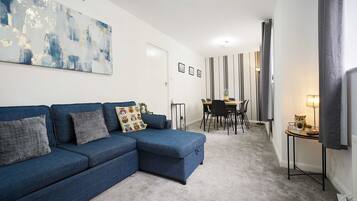 A modern living room with a blue sectional sofa, a dining area with a table and chairs, and a large abstract painting on the wall.