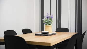 Een vergaderruimte met een houten tafel, zwarte stoelen en een potplant met paarse bloemen.