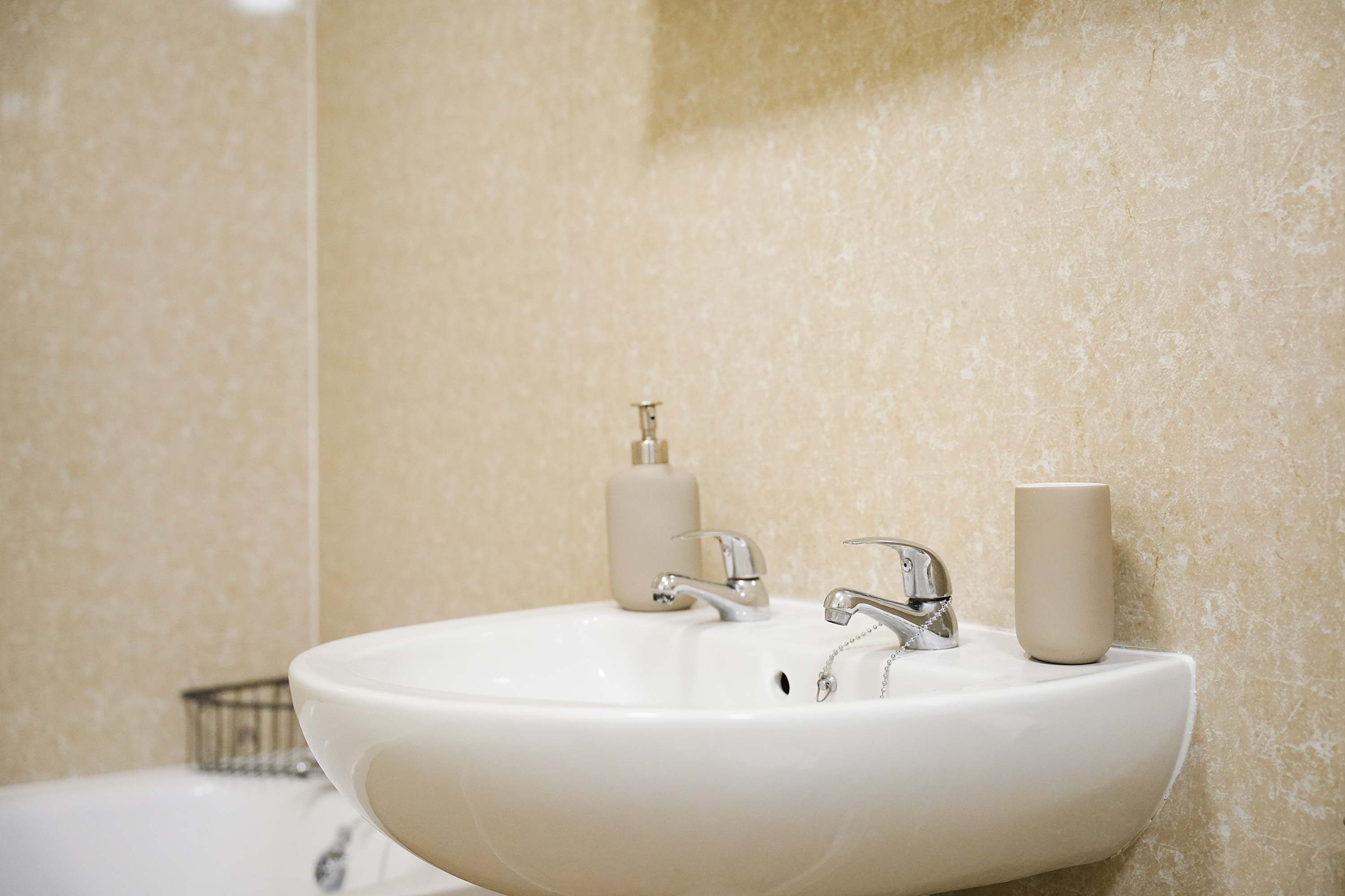 A bathroom with a white sink, two faucets, and a soap dispenser.