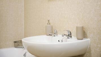 A bathroom with a white sink, two faucets, and a soap dispenser.