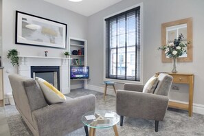 A living room with a fireplace, a television, and a large window with blinds. - Spacious and Comfty 1 Bedroom Haven in Hartlepool (Hartlepool)