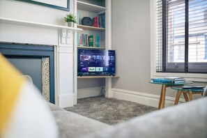 A living room with a fireplace, a television mounted on a wall, and a small table with books. - Spacious and Comfty 1 Bedroom Haven in Hartlepool (Hartlepool)