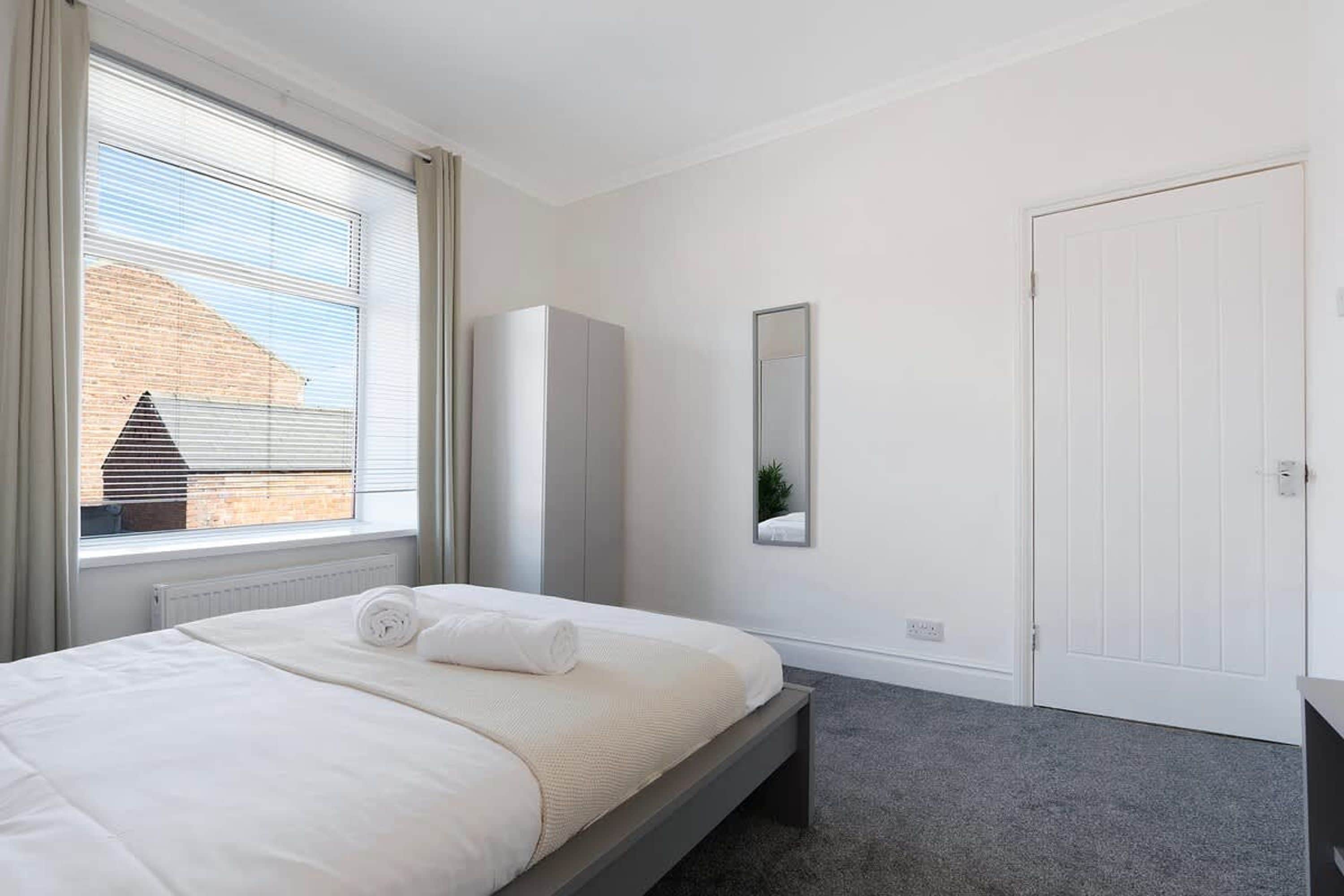 A bedroom with a bed, a wardrobe, a mirror, and a door.