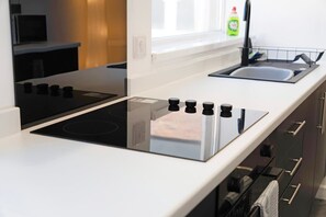 A modern kitchen with a black induction cooktop and a stainless steel sink. - 4BR on Durham Road Perfect For Large Groups (Stanley)