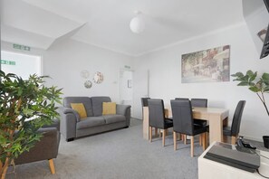 A modern room with a grey sofa, a dining table with chairs, a plant, and a painting on the wall. - 4BR on Durham Road Perfect For Large Groups (Stanley)