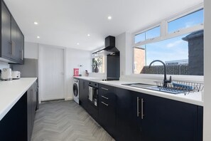A modern kitchen with a built-in washing machine, a large window, and a view of a brick building. - 4BR on Durham Road Perfect For Large Groups (Stanley)