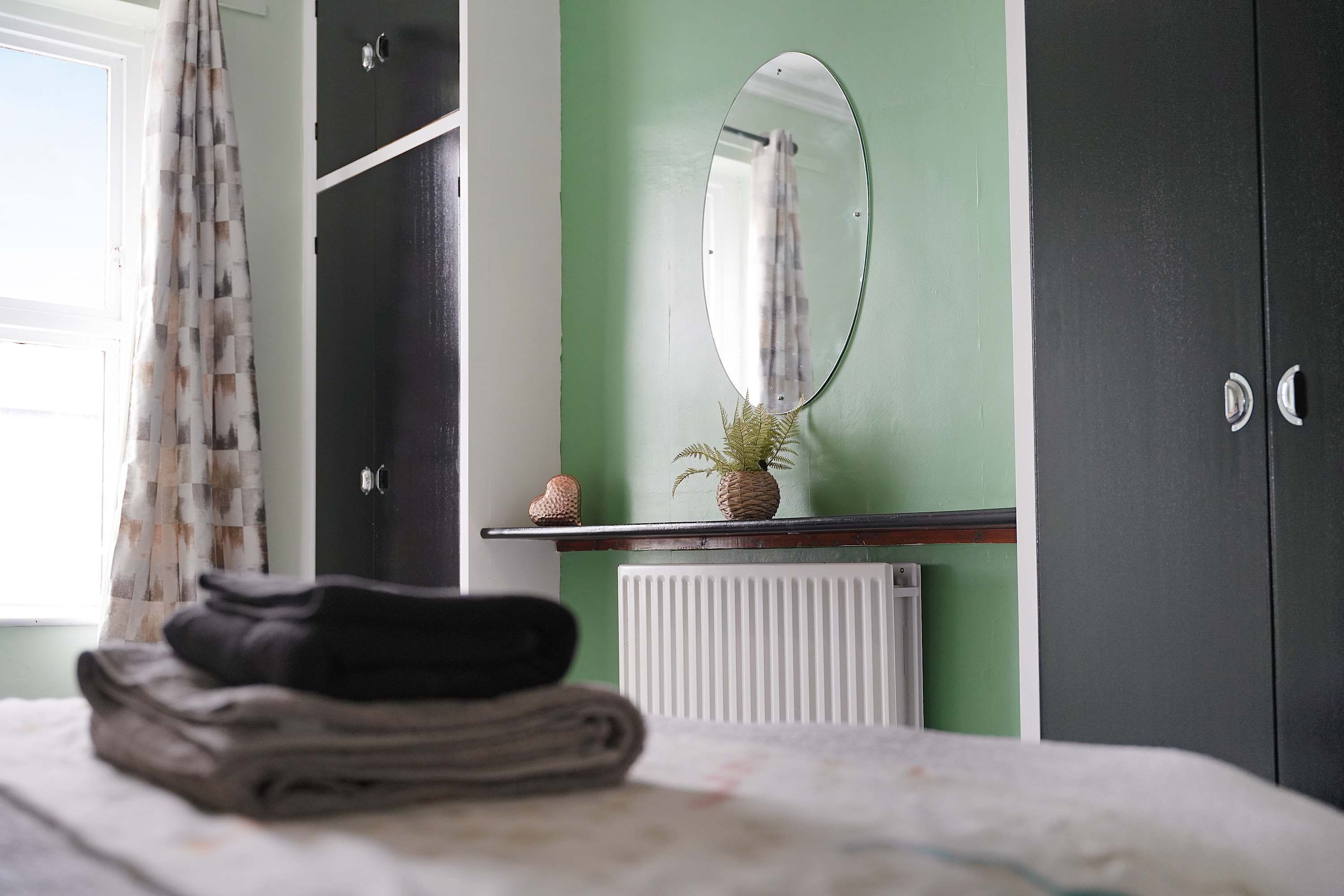 A bedroom with a bed, a radiator, a mirror, and a wardrobe.