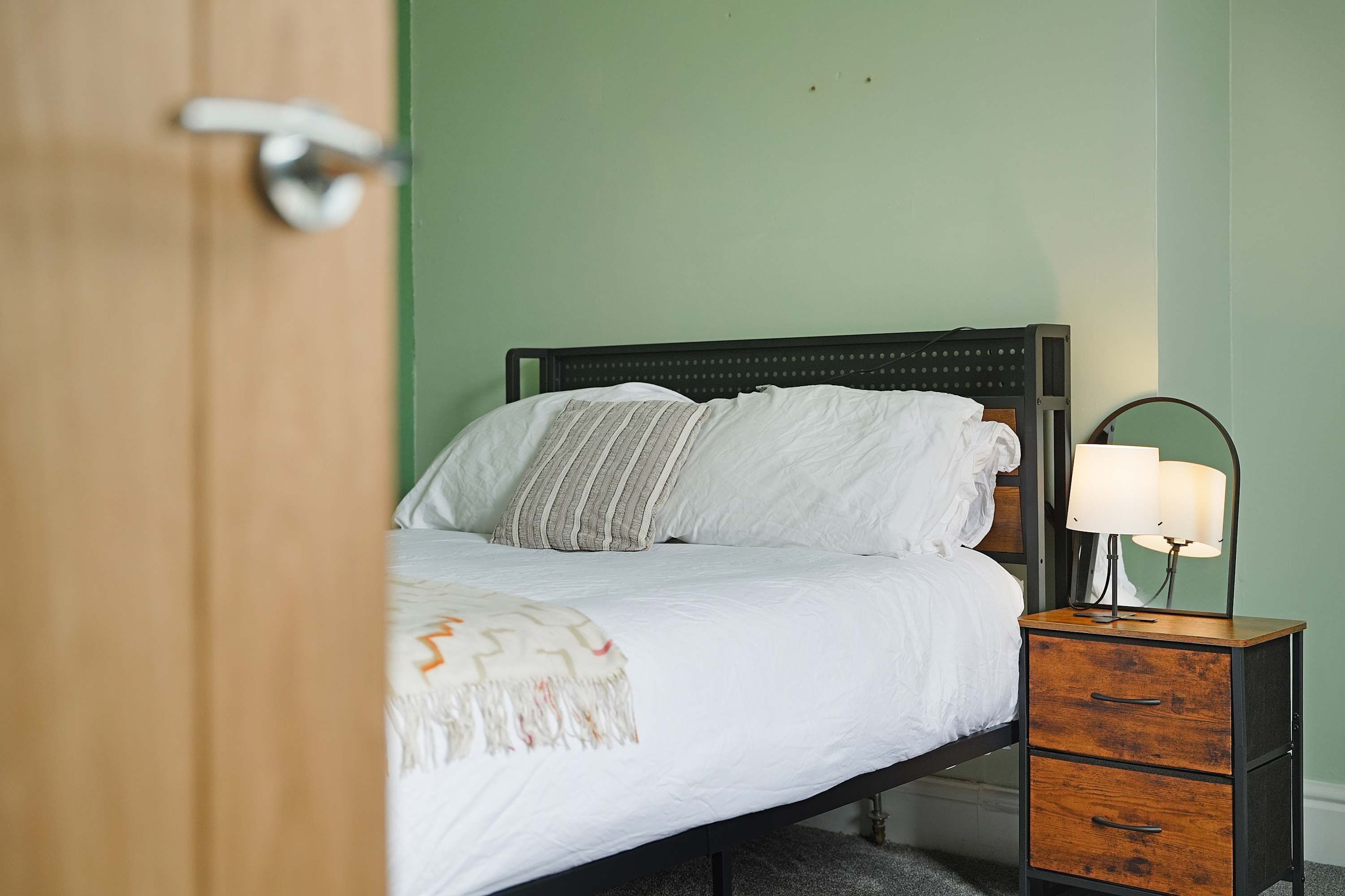 A bedroom with a bed, a bedside table with a lamp, and a wooden nightstand.