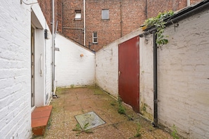 A narrow alleyway with a red door and white walls, leading to a brick building. - The Woodrouffe Retreat (Carlisle)