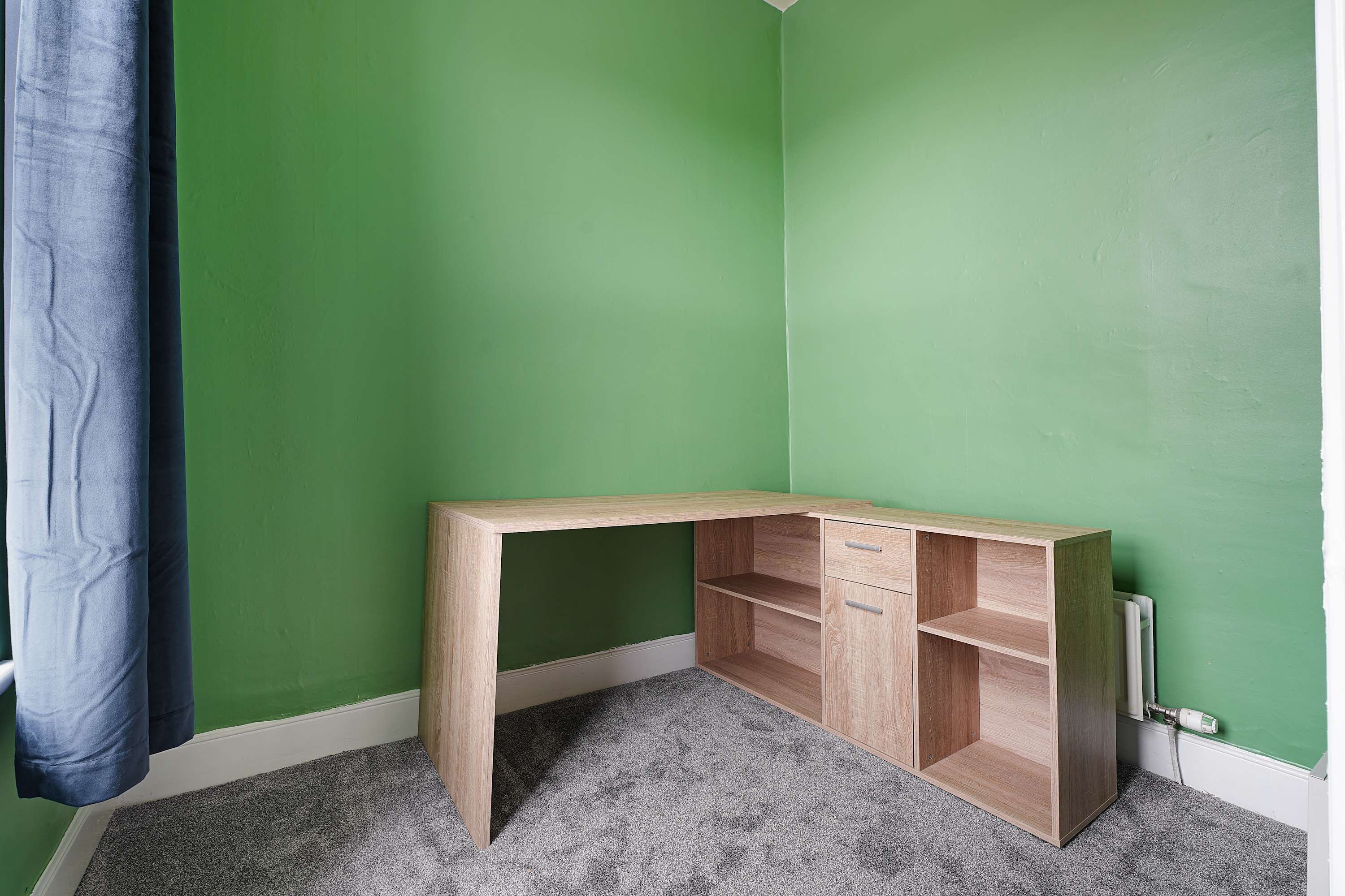 Ein Eckzimmer mit grünen Wänden, einem Holztisch und einem grauen Teppich.