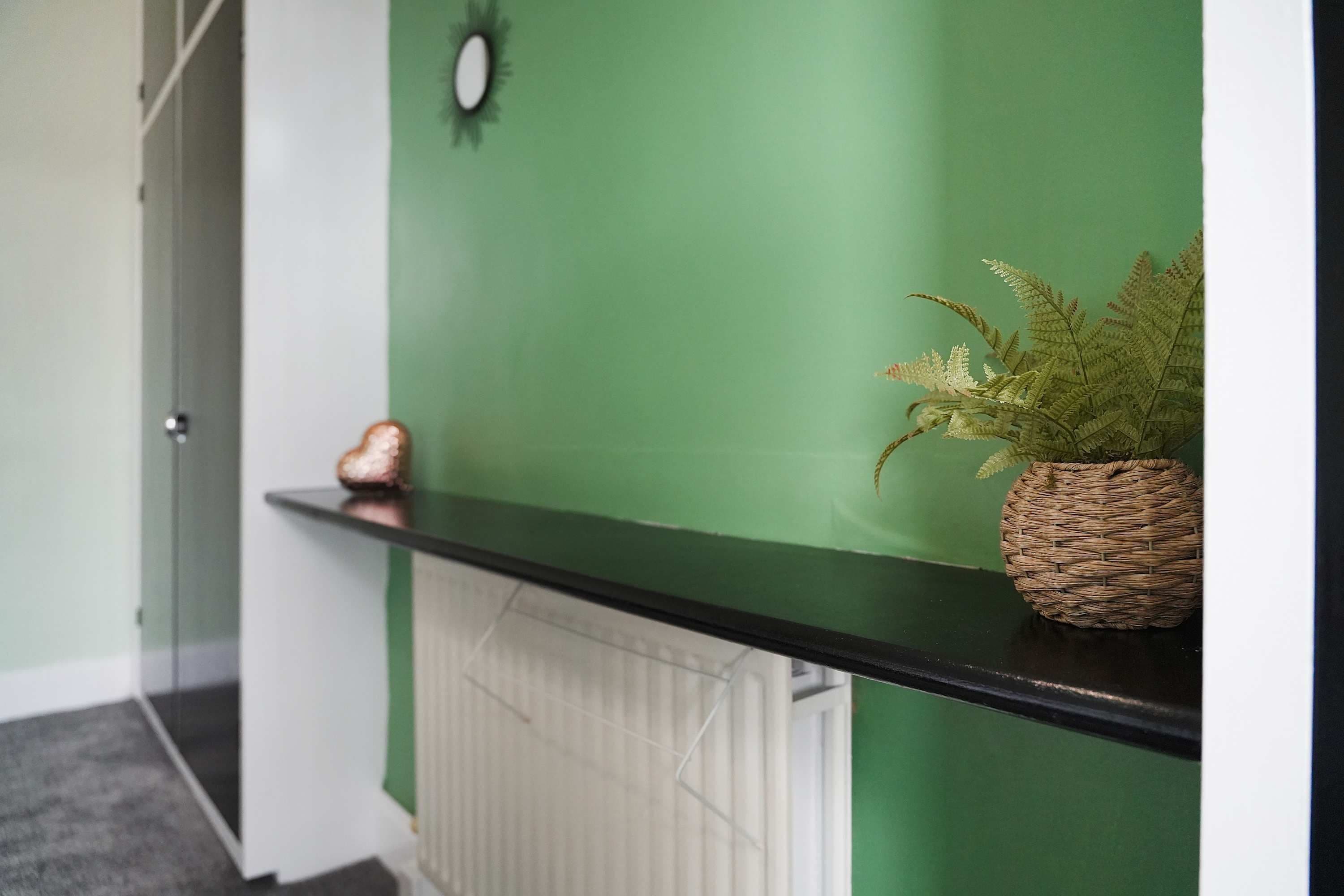 A hallway with a green wall, a black shelf, and a wicker basket with a plant.