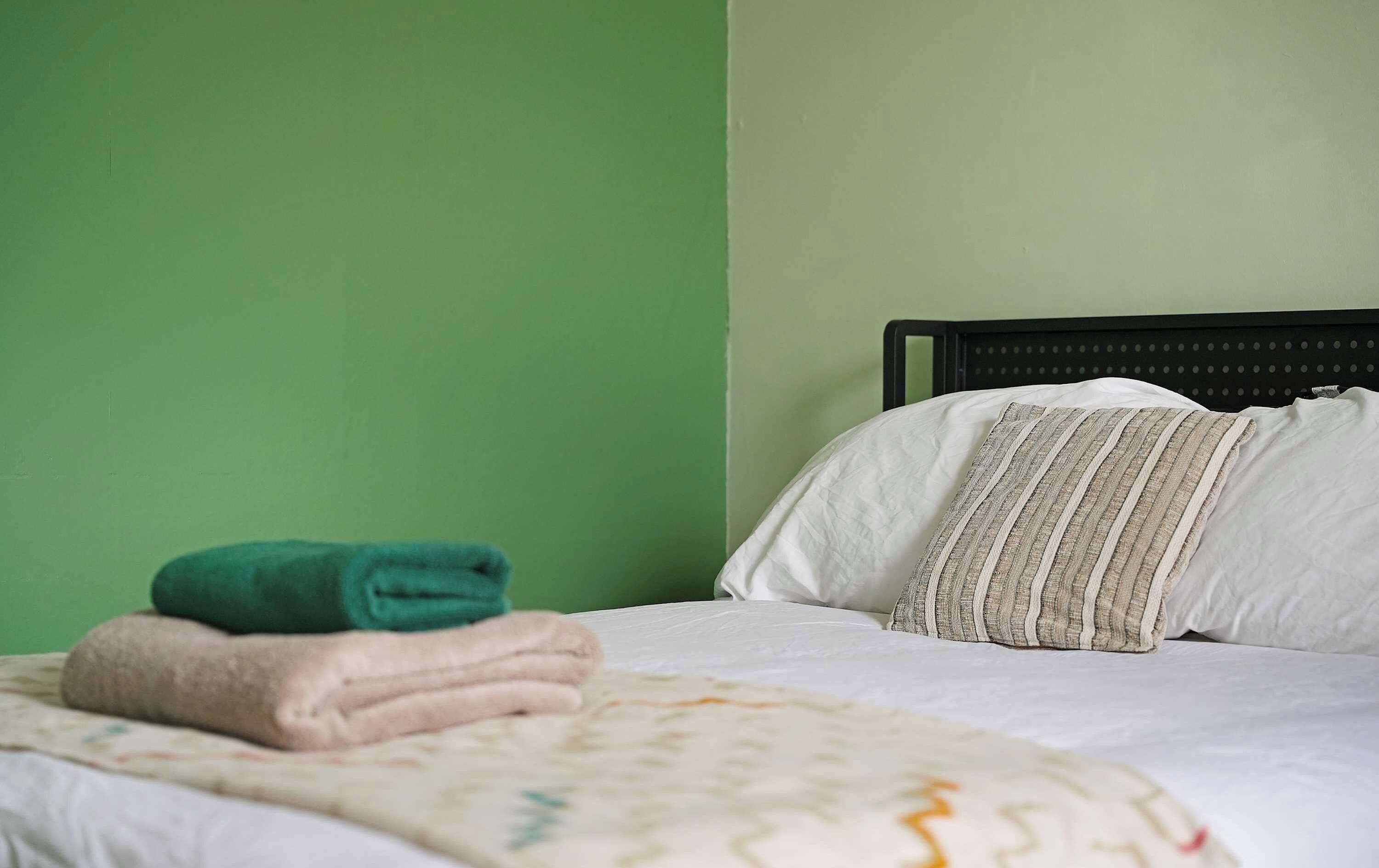 A bed with a white sheet, a green towel, and a patterned pillow.