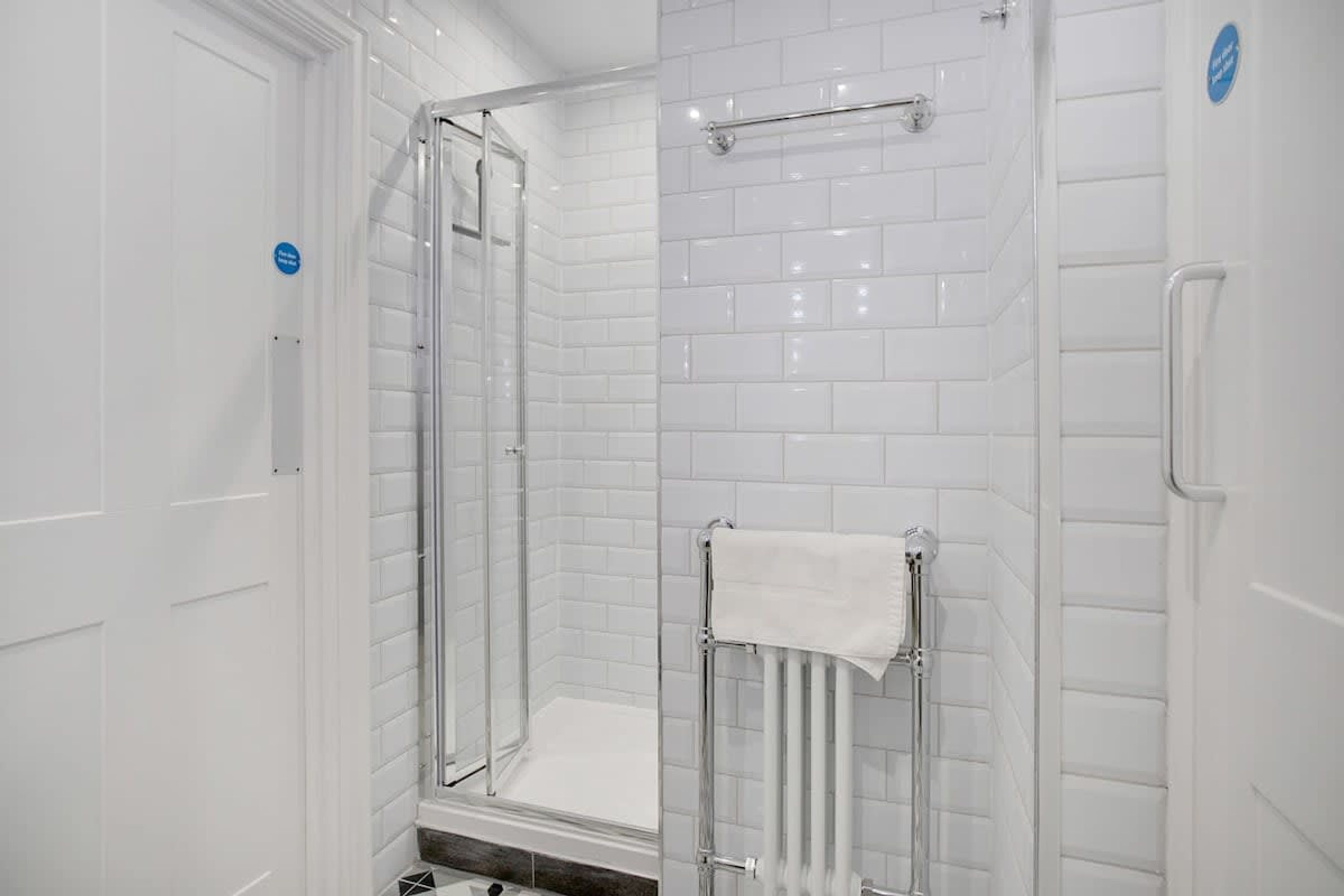 Une salle de bain moderne avec une douche à parois de verre, des murs recouverts de carreaux blancs et un porte-serviettes.