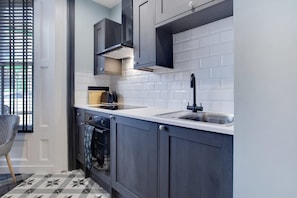 A modern kitchen with dark cabinetry, a white countertop, and a stainless steel sink. - Stylish 1BR Home Near Station by Stay With Us (Hartlepool)