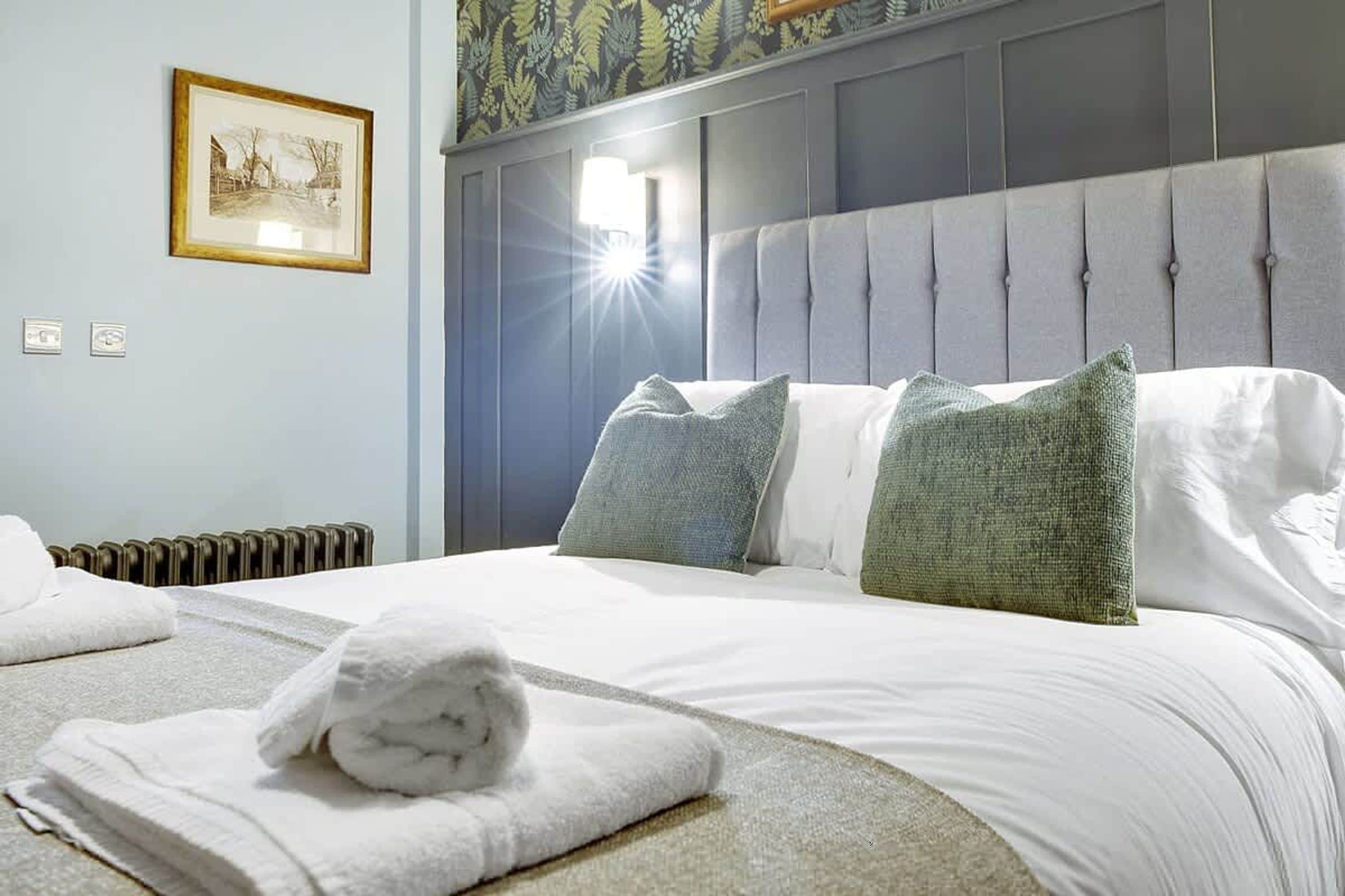 Habitación de hotel con cama, almohadas, radiador y un cuadro en la pared.