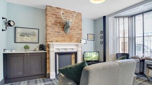 A living room with a fireplace, a sofa, a television, and a brick wall. - Stylish 1BR Home Near Station by Stay With Us (Hartlepool)