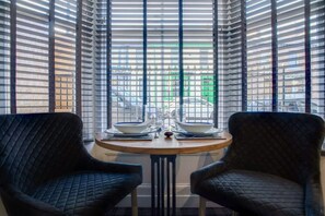 A corner room with two black upholstered chairs, a round wooden table, and a view through a window with horizontal blinds. - Stylish 1BR Home Near Station by Stay With Us (Hartlepool)