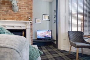 A living room with a fireplace, a television, a plaid carpet, and a chair. - Stylish 1BR Home Near Station by Stay With Us (Hartlepool)