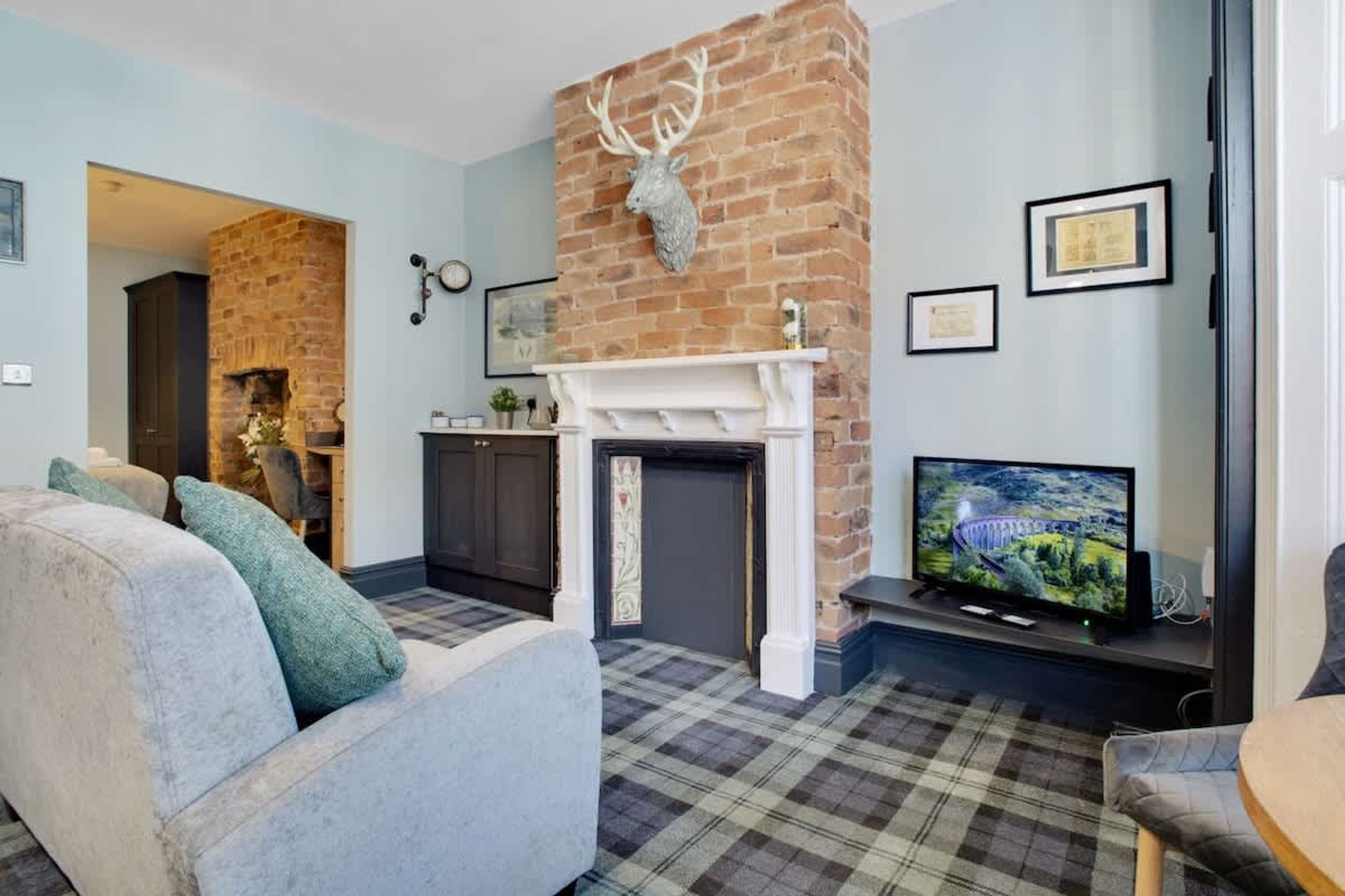 A living room with a fireplace, a television, and a plaid carpet.