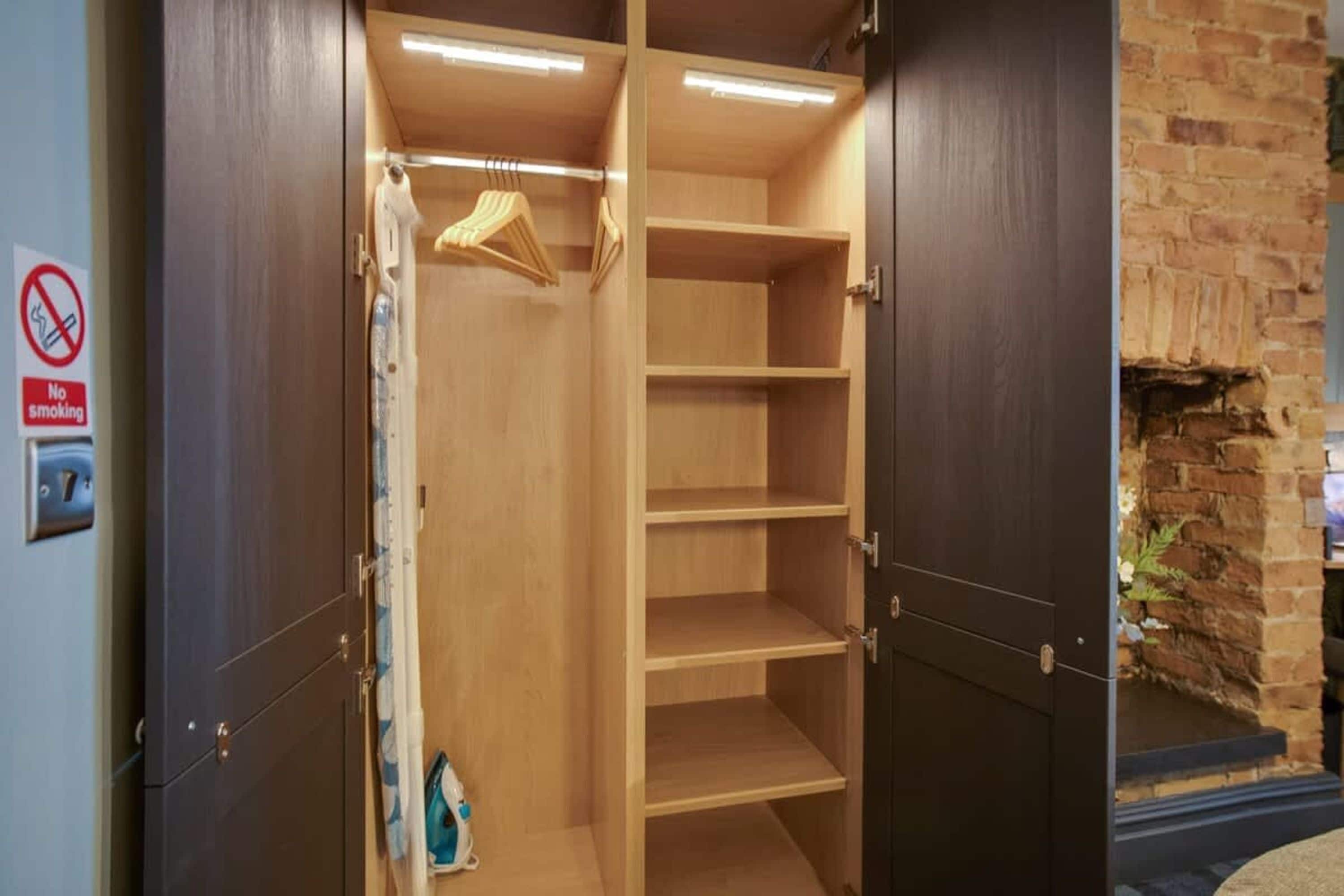 A walk-in closet with wooden shelves and a hanging rod, a no-smoking sign on the wall, and a brick fireplace.