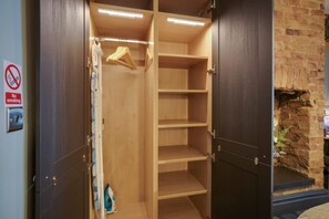 A walk-in closet with wooden shelves and a hanging rod, a no-smoking sign on the wall, and a brick fireplace. - Stylish 1BR Home Near Station by Stay With Us (Hartlepool)