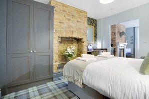 Quarto com cama grande, guarda-roupa cinzento, parede de tijolos e lareira.