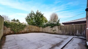 Un pati de formigó amb una tanca de fusta, un garatge i un gran arbre de fulles perennes.