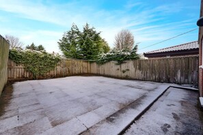 Ein Hinterhof aus Beton mit Holzparkanlage, einer Garage und einem großen immergrünen Baum.