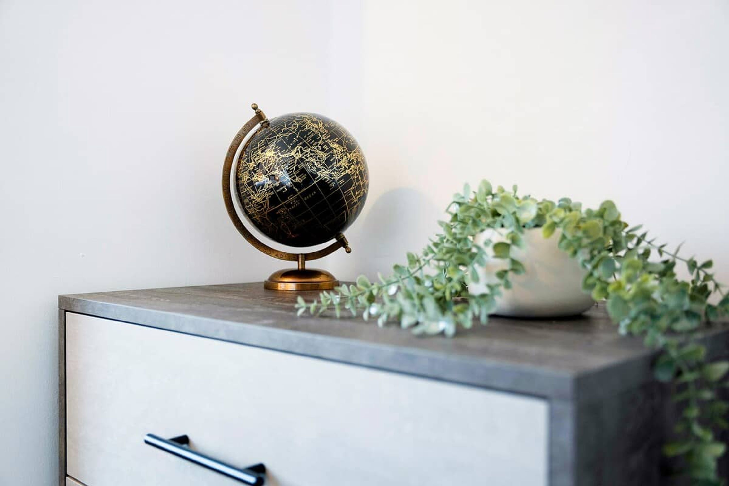 Un globe terrestre posé sur un bureau, avec un tiroir et une plante à côté.