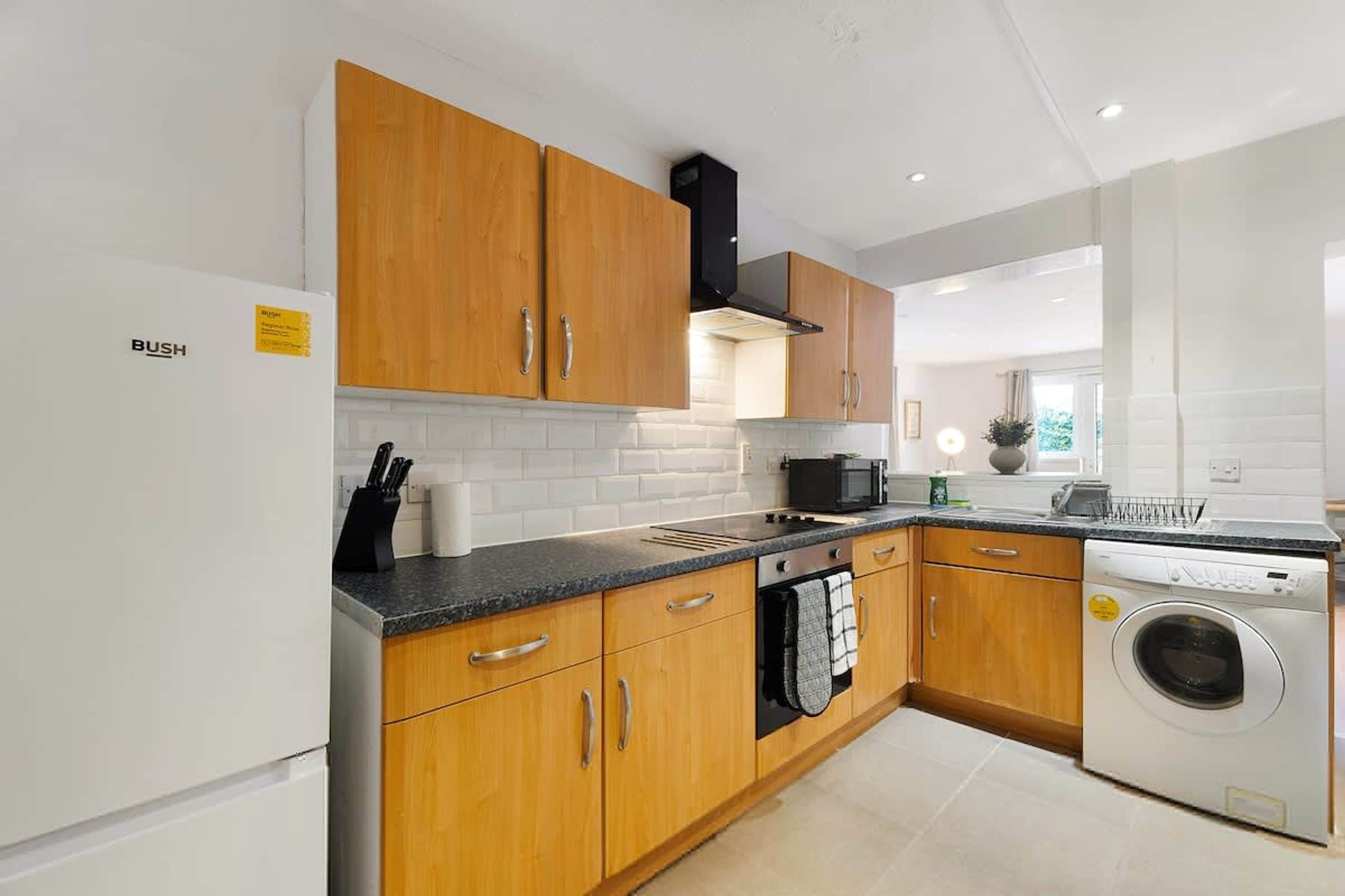 A modern kitchen with wooden cabinets, a built-in oven, a microwave, and a washing machine.