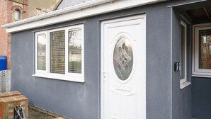 Una casa de fachada gris, con una puerta blanca y un panel de vidrio decorativo, y una ventana con persianas.