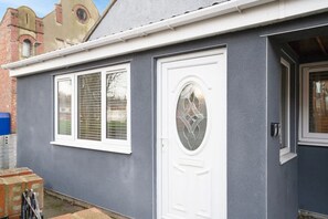 Ein Haus mit grauer Fassade, einer weißen Tür mit dekorativem Glasfenster und einem Fenster mit Rollläden.