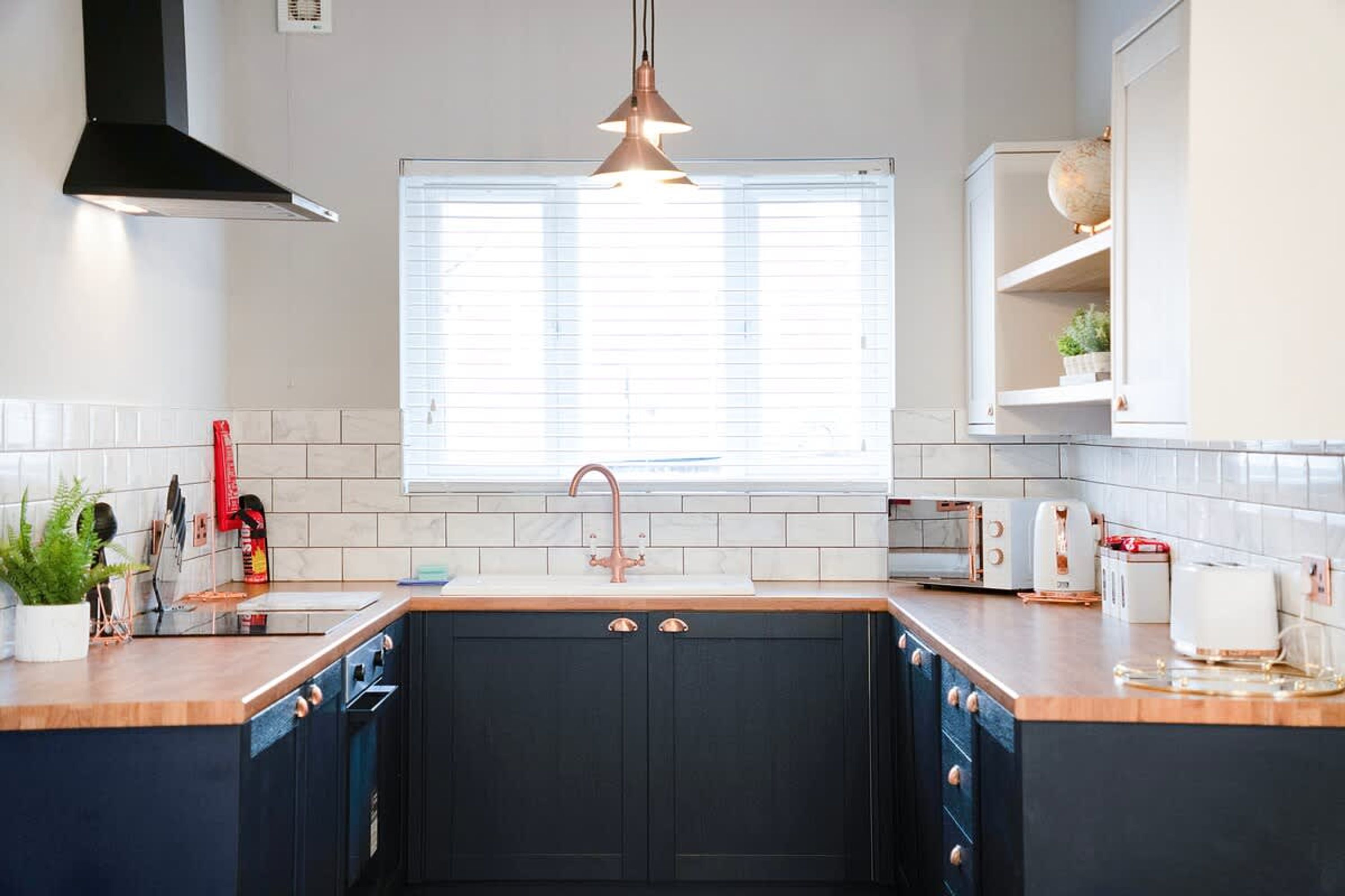 A modern kitchen with a central island, a sink with a copper faucet, and a window with blinds.
