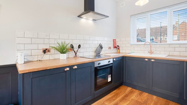 Una cocina moderna con armarios oscuros, encimera de madera, horno integrado y una ventana con persianas.